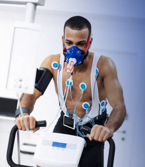 Sportlicher junger Mann sitzt verkabelt und mit Atemmaske auf einem Cardio-Fahrrad